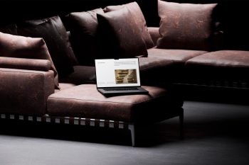 Wide shot of a laptop in a designed room featuring leather furniture, concrete walls, and artistic shadows.
